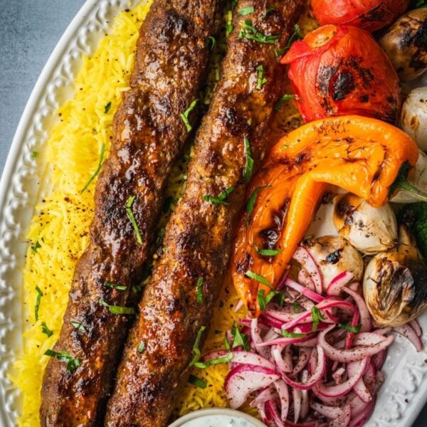 A platter with saffron rice, grilled koobideh kebabs, grilled vegetables and sumac onions.