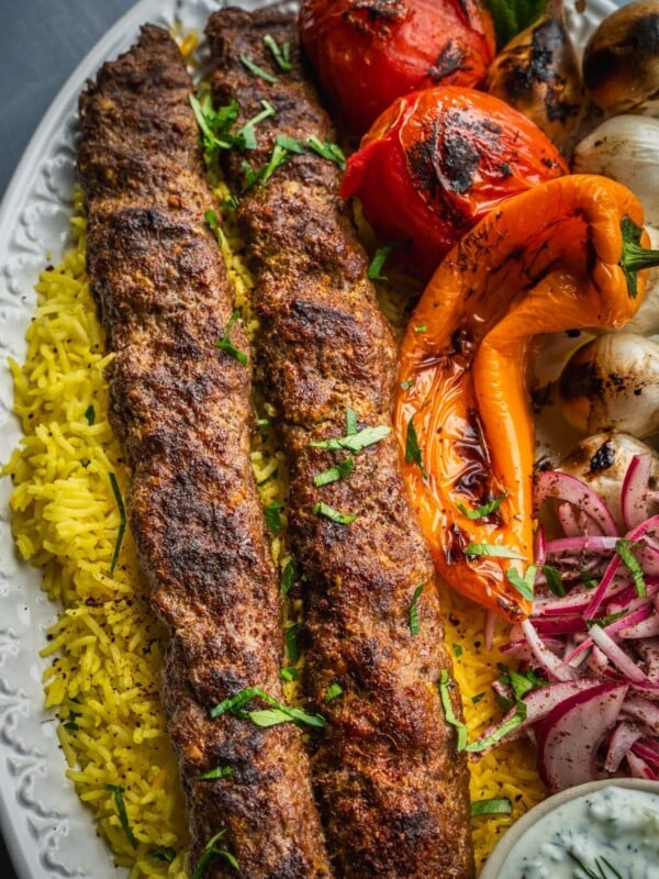 A platter with saffron rice, grilled koobideh kebabs, grilled vegetables and sumac onions.