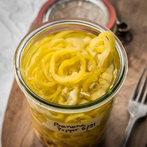 An open jar of pickled banana peppers on a wooden board.