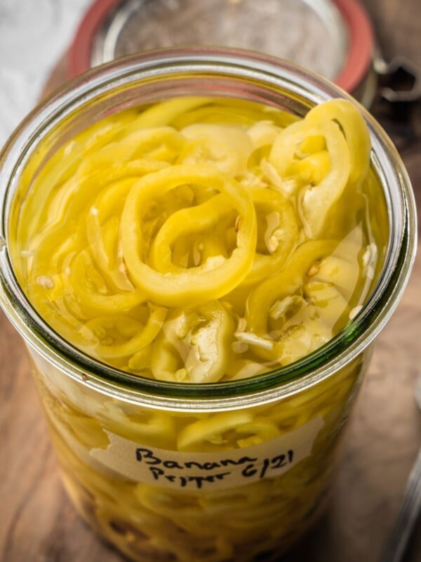 An open jar of pickled banana peppers on a wooden board.