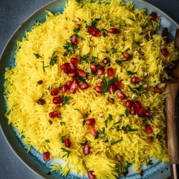 A plate with saffron rice garnished with pomegranate seeds, parsley and nuts.