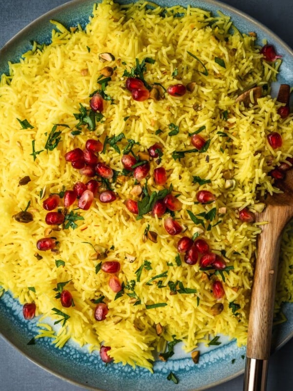 A plate with saffron rice garnished with pomegranate seeds, parsley and nuts.