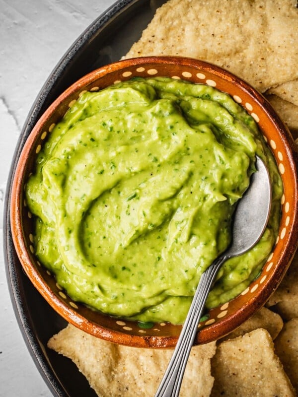 Avocado salsa in a bowl with a spoon and nacho chips on the side.
