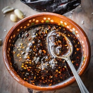 Salsa macha in a terracotta bowl with a spoon on a wooden board.