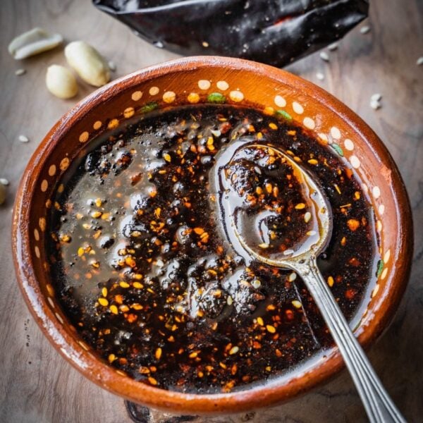 Salsa macha in a terracotta bowl with a spoon on a wooden board.