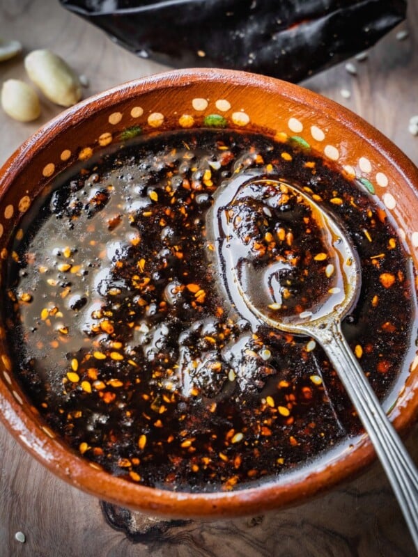 Salsa macha in a terracotta bowl with a spoon on a wooden board.