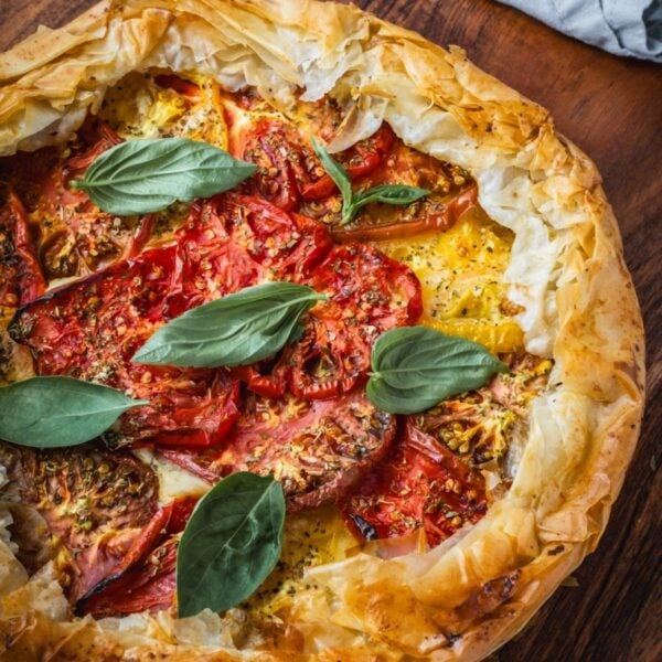 Cheese and tomato pie on a wooden board garnished with basil.