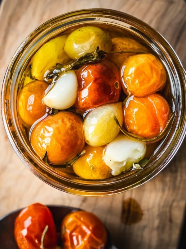 A jar of confit cherry tomatoes on a board.