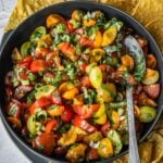 Cherry tomato salsa in a bowl with a spoon and a side of tortilla chips.