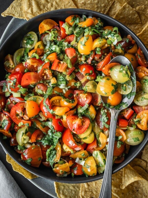 Cherry tomato salsa in a bowl with a spoon and a side of tortilla chips.
