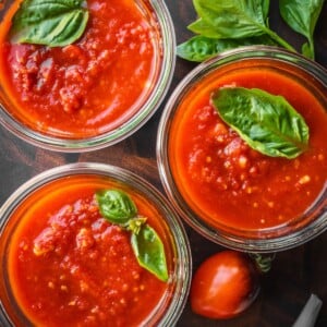 Marinara sauce in mason jars garnished with fresh basil leaves.