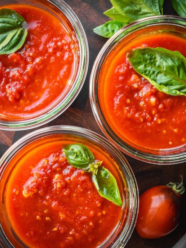 Marinara sauce in mason jars garnished with fresh basil leaves.