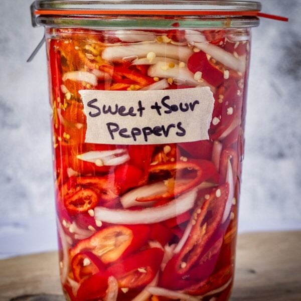 Sealed and labeled jar of pickled sweet peppers on a wooden board.