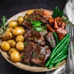 Sliced Braised Chuck Roast on a platter with potatoes, carrots and green beans.