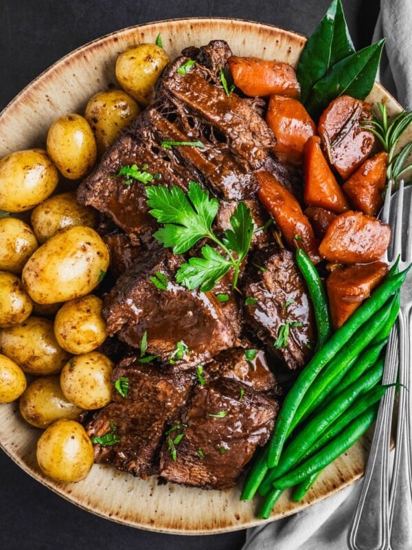 Sliced Chuck Roast on a platter with potatoes, carrots and green beans.