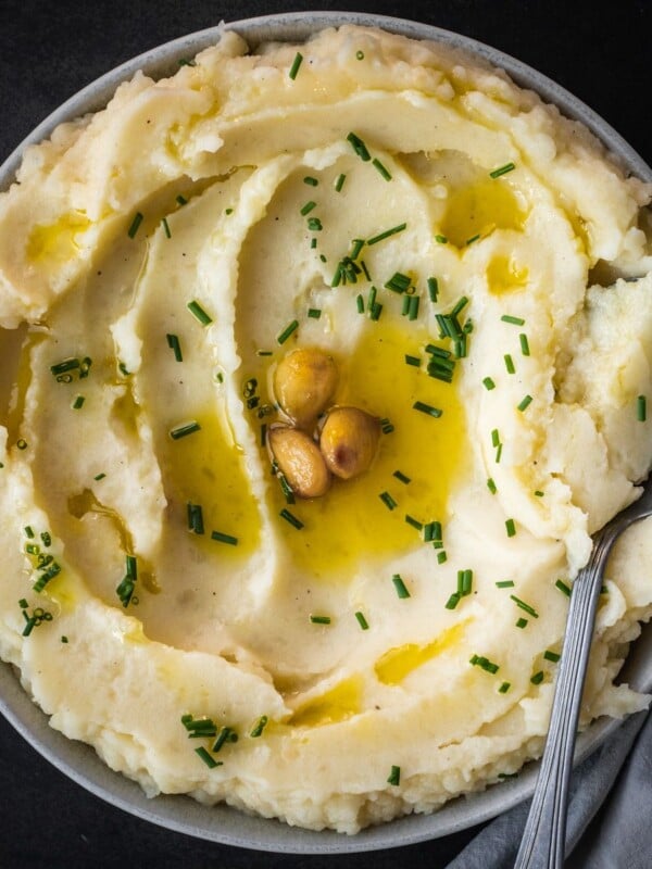 Garlic confit mashed potatoes in a bowl garnished with chives and more garlic cloves.