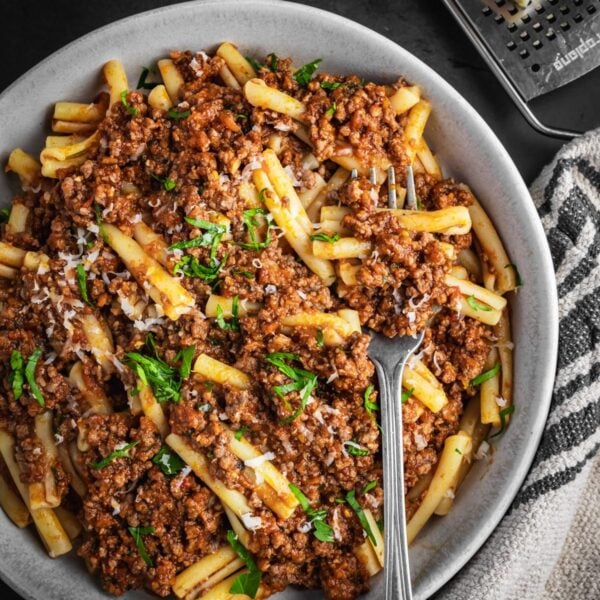 Plated bowl of beef Bolognese with pasta, parsley and parmesan cheese.