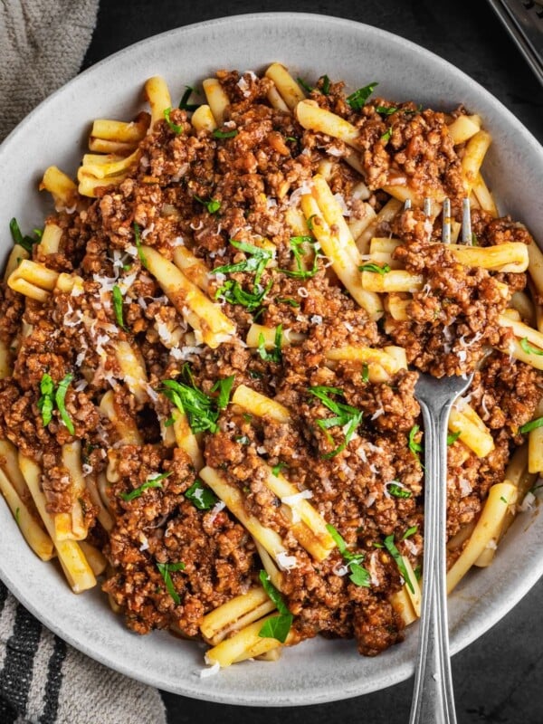 Plated bowl of beef Bolognese with pasta, parsley and parmesan cheese.