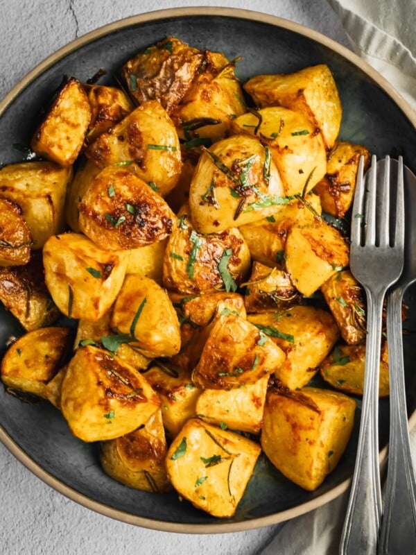 Bowl of garlic and rosemary roasted potatoes with parsley garnish.