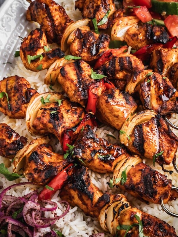 A platter with rice, chopped salad, sumac onions and harissa chicken skewers.