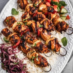 A platter with rice, chopped salad, sumac onions and harissa chicken skewers.