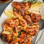 Harissa hot honey chicken pieces on a platter with fresh thyme and lemon wedges.