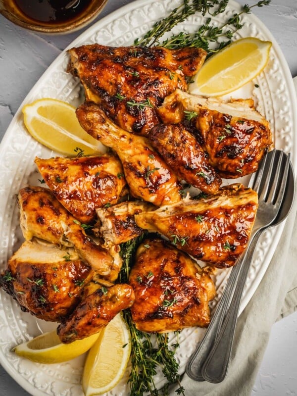 Harissa honey chicken pieces on a platter with fresh thyme and lemon wedges.