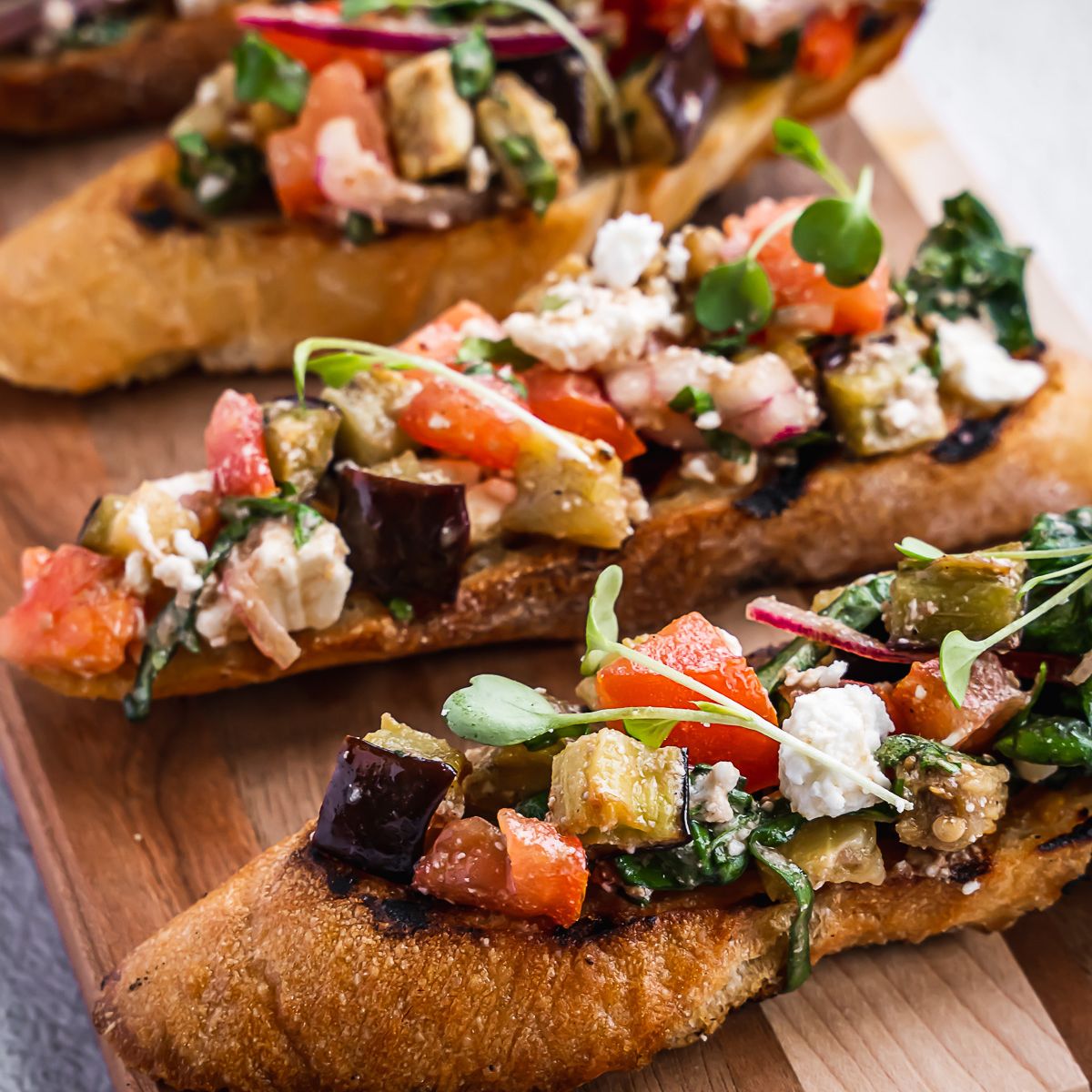 Eggplant and tomato bruschetta on a wooden board.