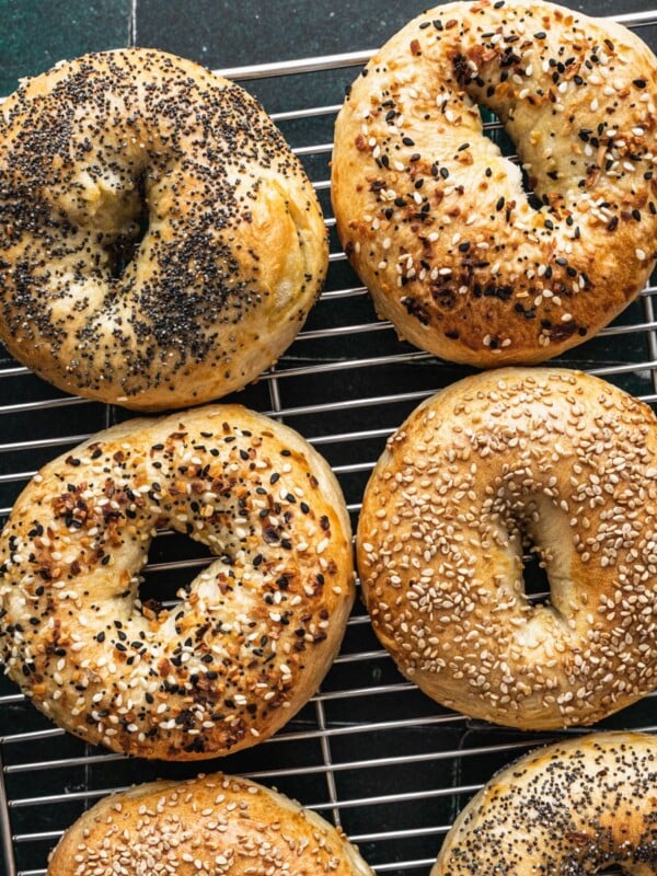 New York bagels on a cooling rack with various toppings including sesame seeds, everything bagel and poppy seeds.