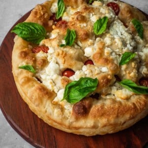 Feta and cherry tomato focaccia garnished with fresh basil on a board.