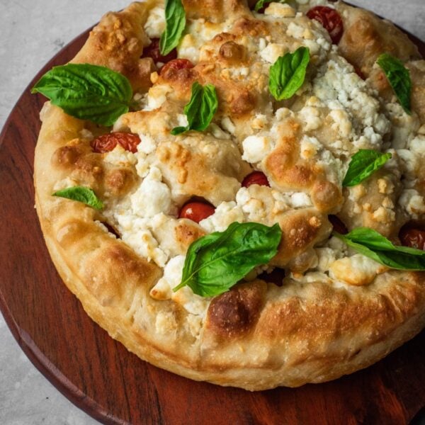 Feta and cherry tomato focaccia garnished with fresh basil on a board.