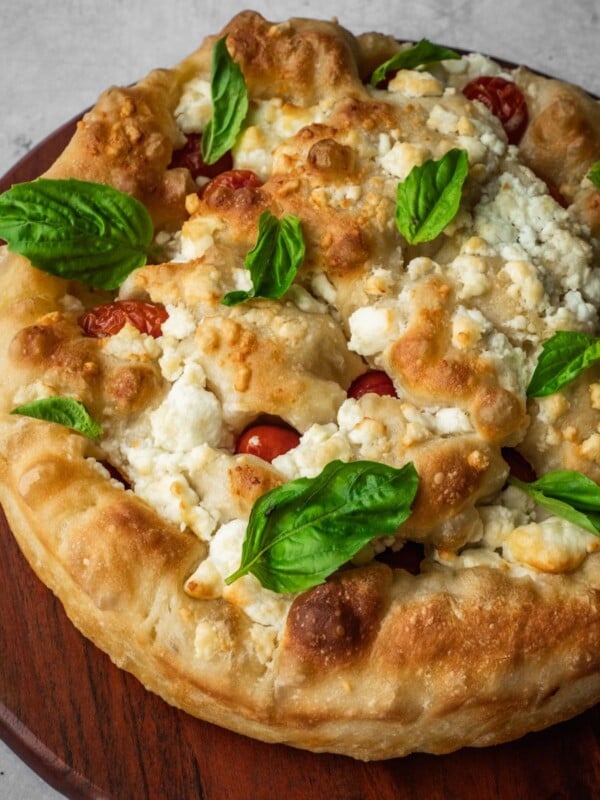 Feta and cherry tomato focaccia garnished with fresh basil on a board.