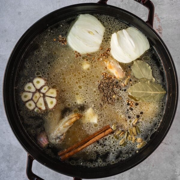 Middle Eastern Style Chicken broth ingredients in a large Dutch oven with seared chicken, water, and aromatics.