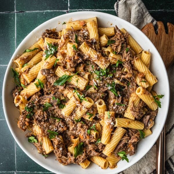 Pasta alla Genovese in a serving bowl garnished with parsley with parmesan cheese on the side.