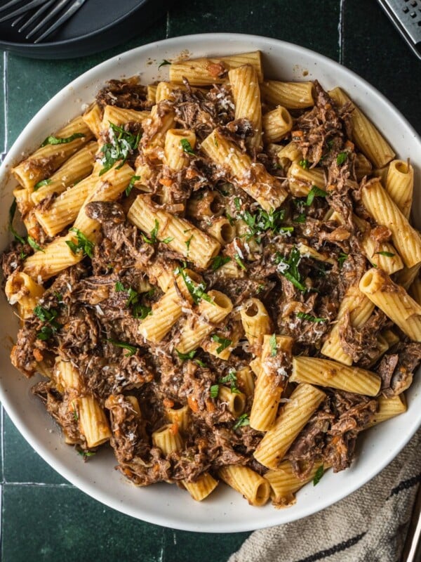 Pasta alla Genovese in a serving bowl garnished with parsley with parmesan cheese on the side.