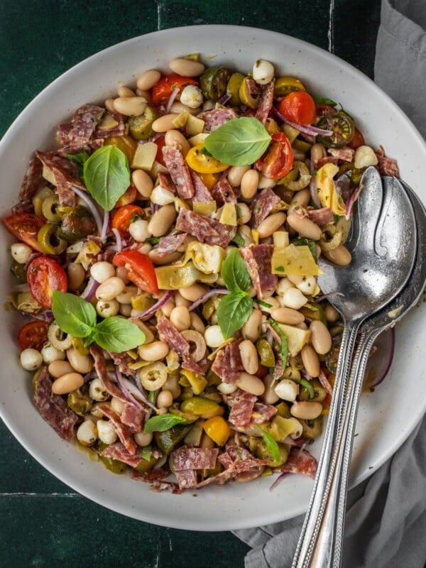 Bean antipasto salad with salami, cherry tomatoes, fresh basil garnish in a bow.