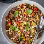 Bean antipasto salad with salami, cherry tomatoes, fresh basil garnish in a bow.