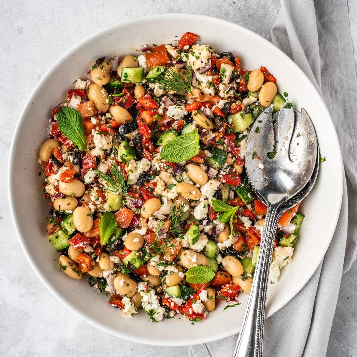 A bowl with a Greek style bean salad including butter beans, cucumbers tomatoes, olives and herbs.