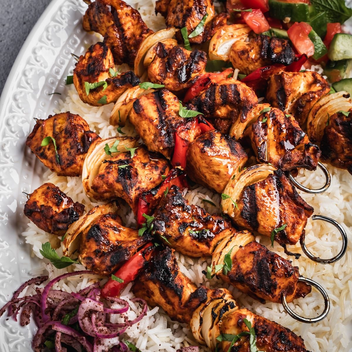 Platter with chicken breast skewers with grilled onion and bell pepper on a bed of rice.