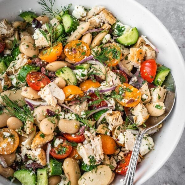 Greek chicken salad with butter beans, cherry tomatoes, feta and cucumbers garnished with fresh dill fronds in a large serving bowl.