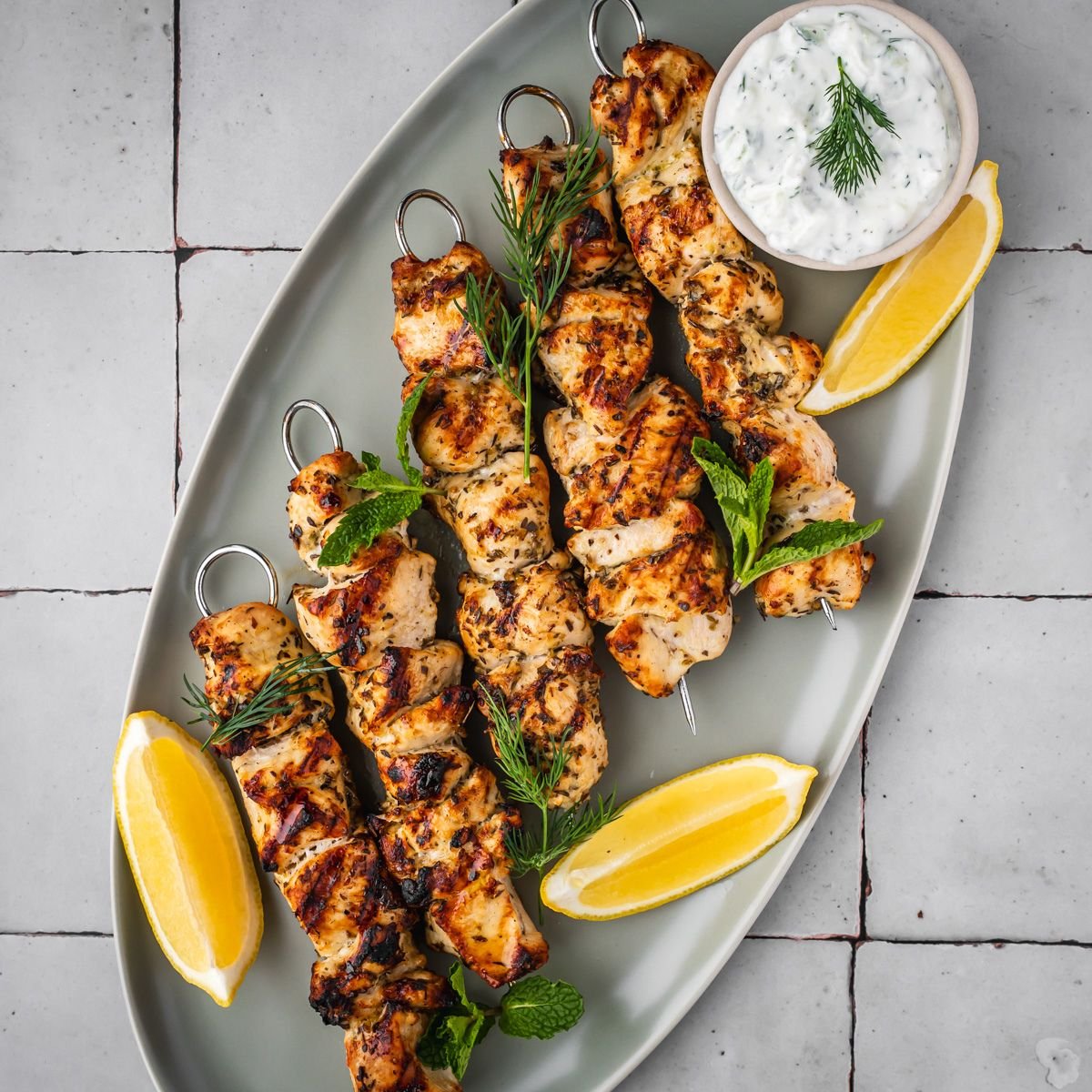 Platter with Greek chicken souvlaki skewers garnished with dill and mint.