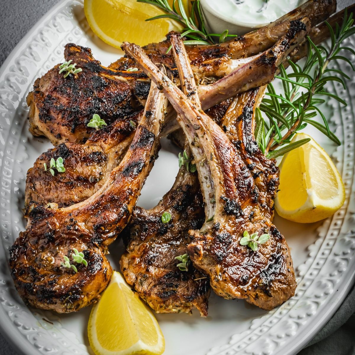 Platter with grilled lamb chops garnished with herbs and lemon.