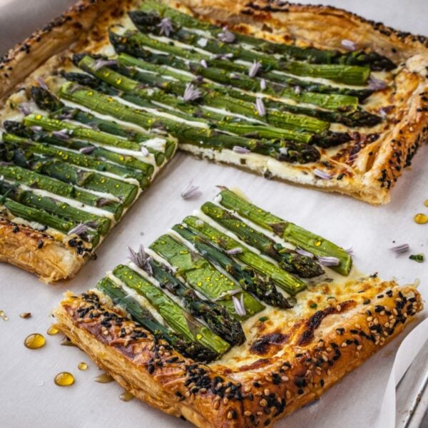 Asparagus goat cheese puff pastry tart on a baking sheet garnished with chive flowers and honey.