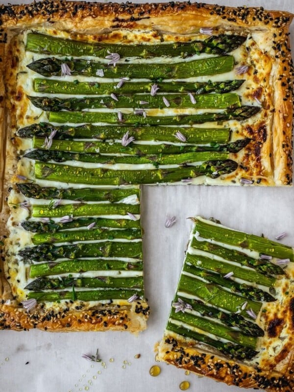 Asparagus goat cheese puff pastry tart on a baking sheet garnished with chive flowers and honey.
