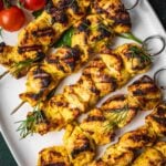 Grilled Joojeh Kabob chicken skewers with a golden char served on a white platter, garnished with fresh dill, cherry tomatoes.