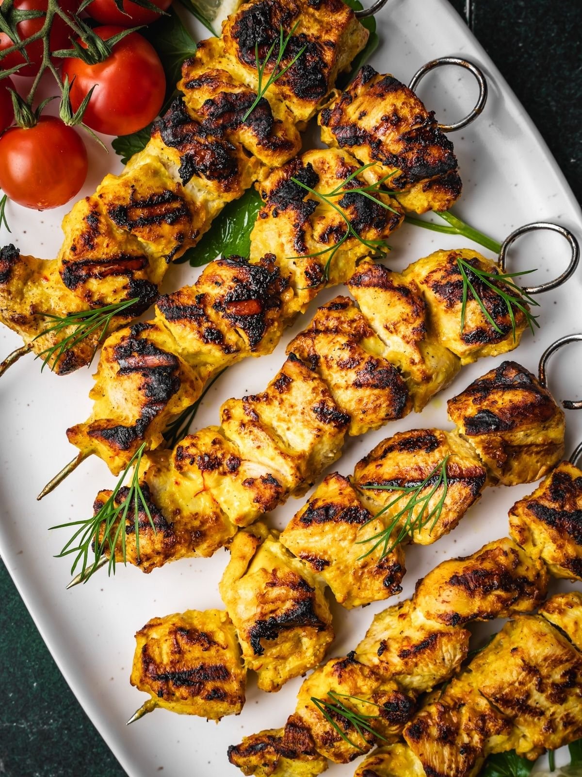 Grilled Joojeh Kabob chicken skewers with a golden char served on a white platter, garnished with fresh dill, cherry tomatoes.