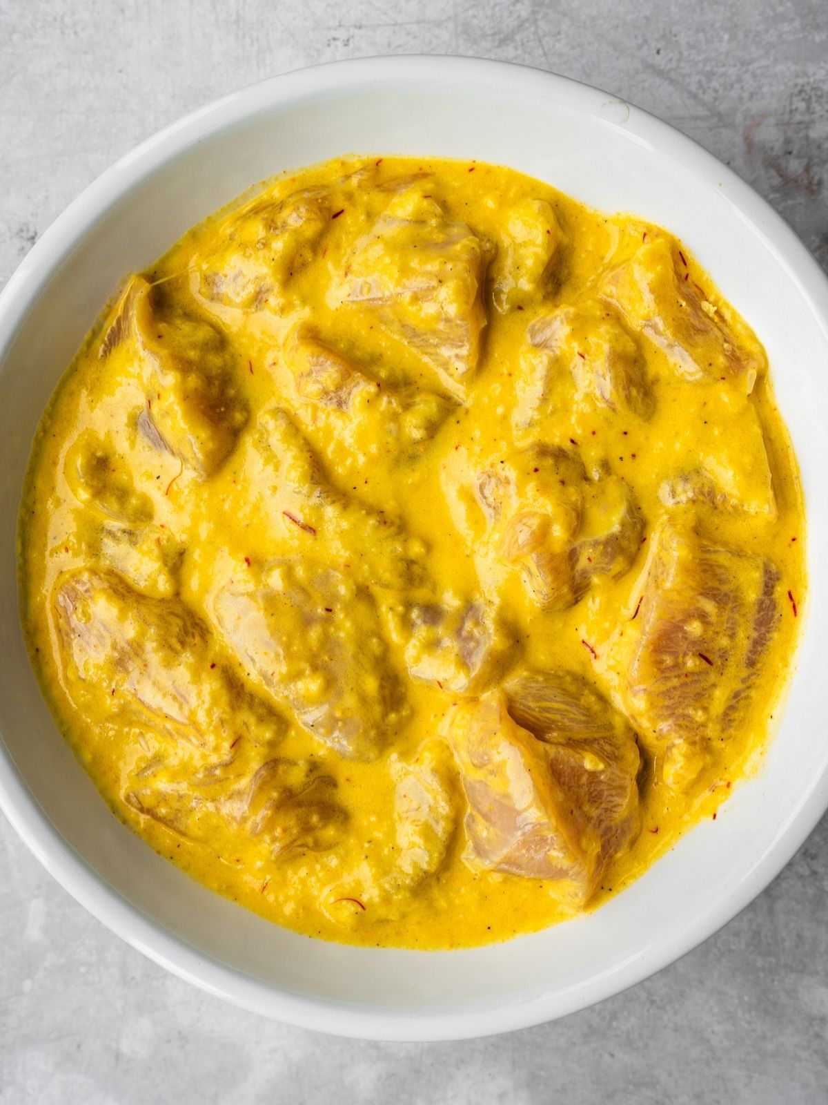A bowl with chicken cubes marinating in the Joojeh kabob marinade.