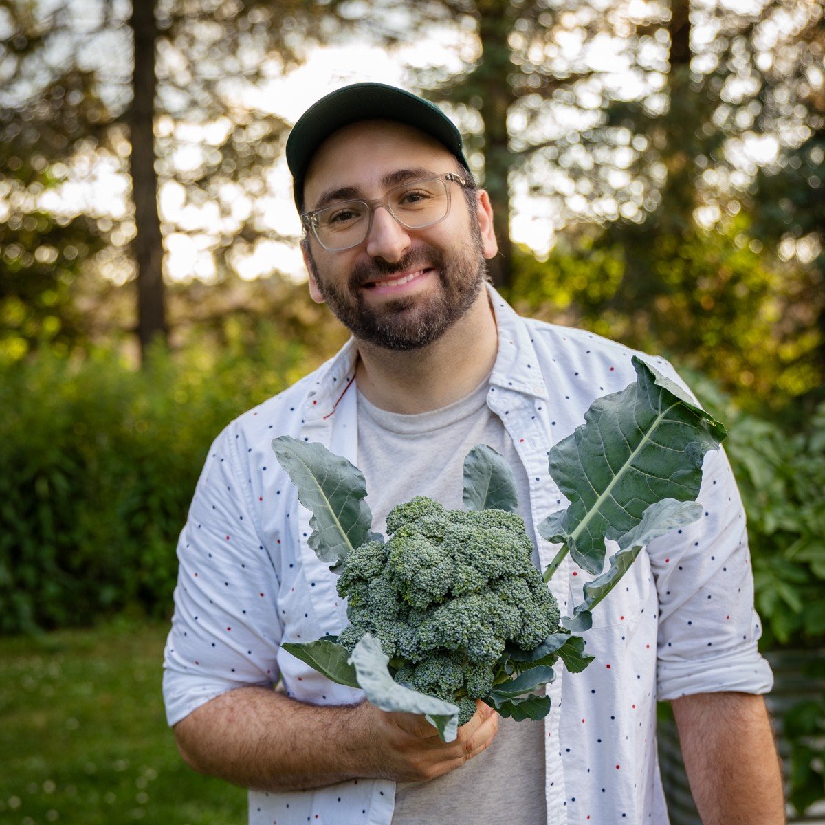 Luay Ghafari holding a broccoli in a garden.