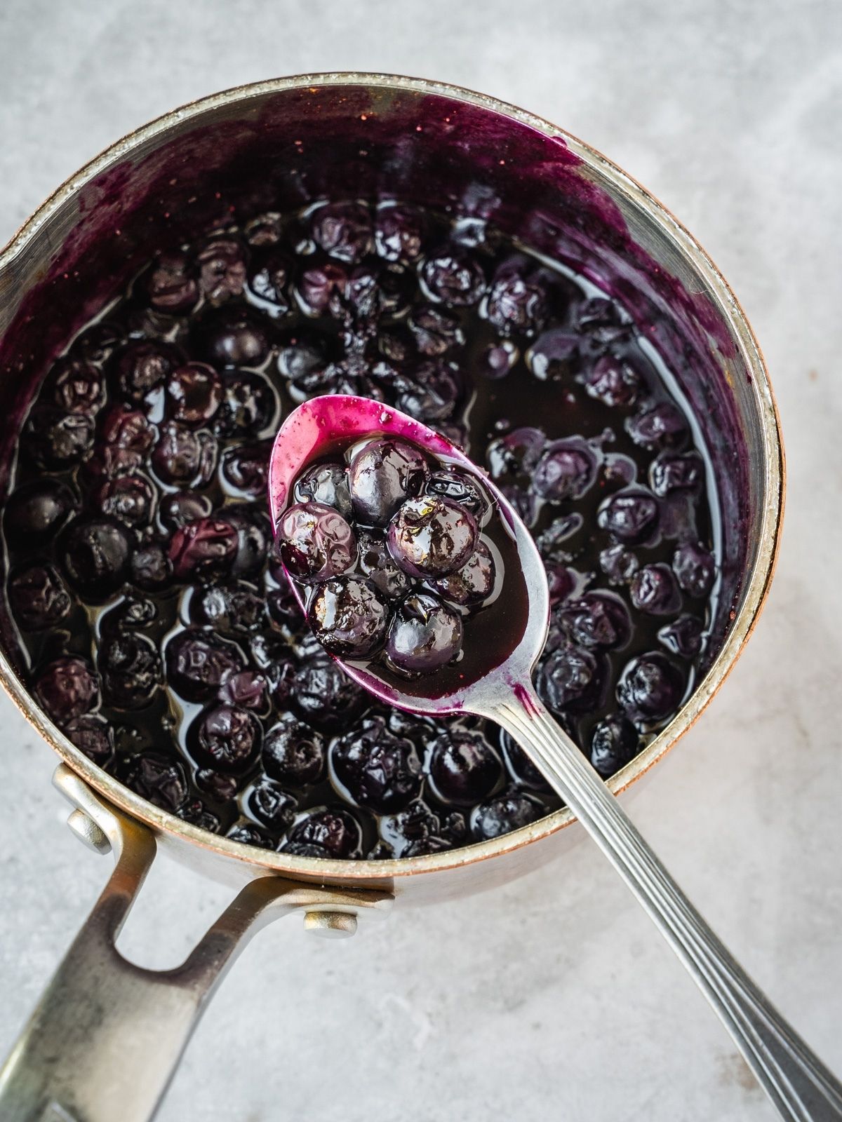 Blueberry Maple Compote in a saucepan with a spoon.