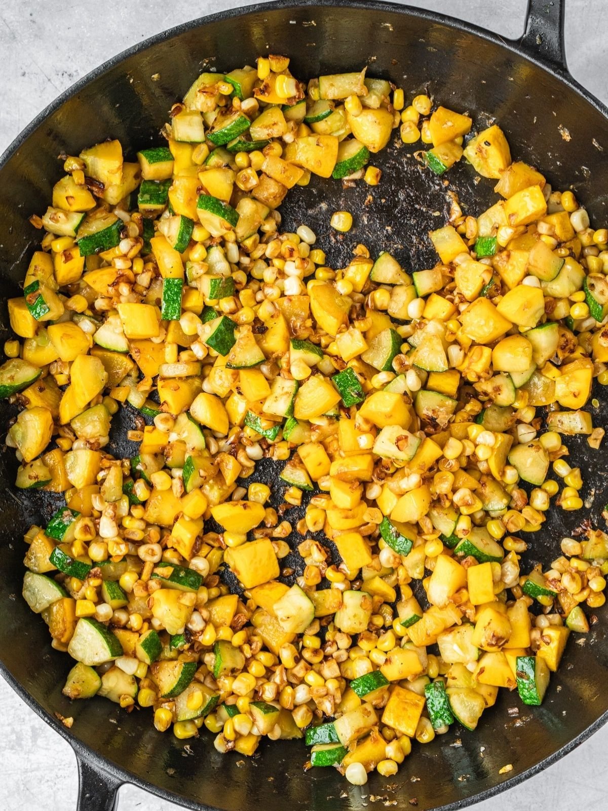 Corn and zucchini chunks frying in a sauté pan.